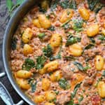 creamy sausage gnocchi with spinach and tomato sauce in a stainless steel pan