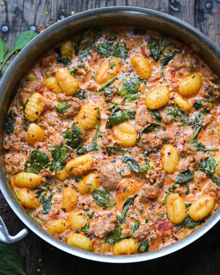 creamy sausage gnocchi with spinach and tomato sauce in a stainless steel pan