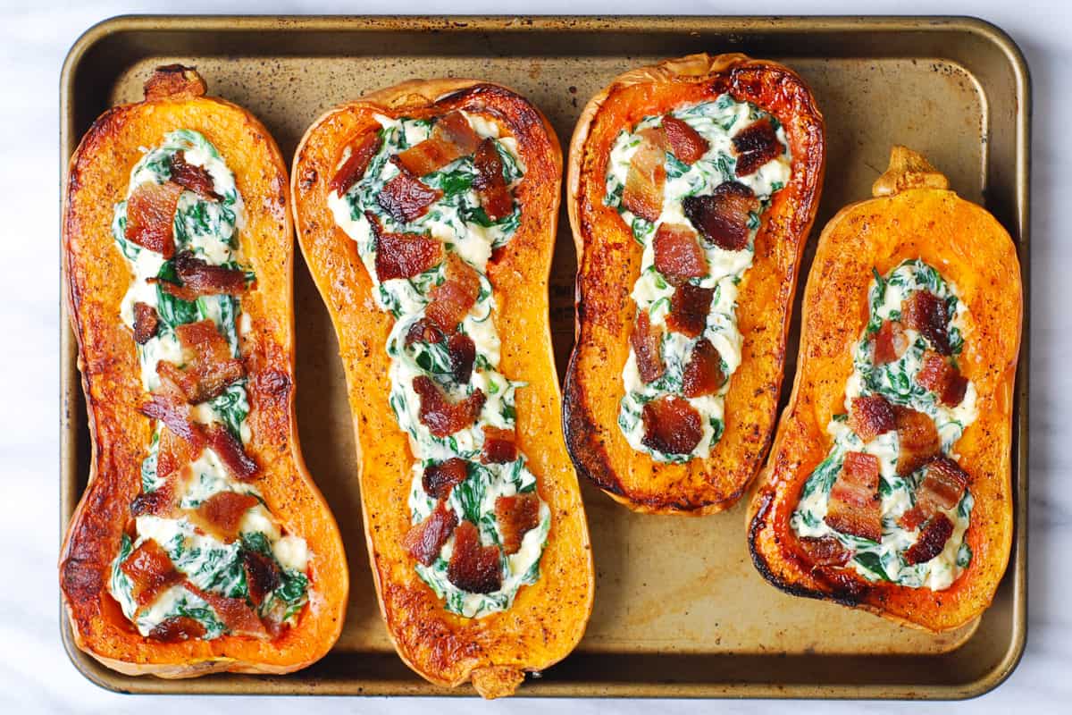 roasted butternut squash stuffed with spinach and cheese and chopped cooked bacon on top on a baking sheet