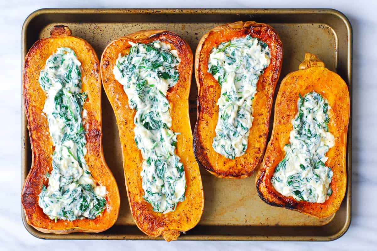 roasted butternut squash stuffed with spinach and cheese on a baking sheet