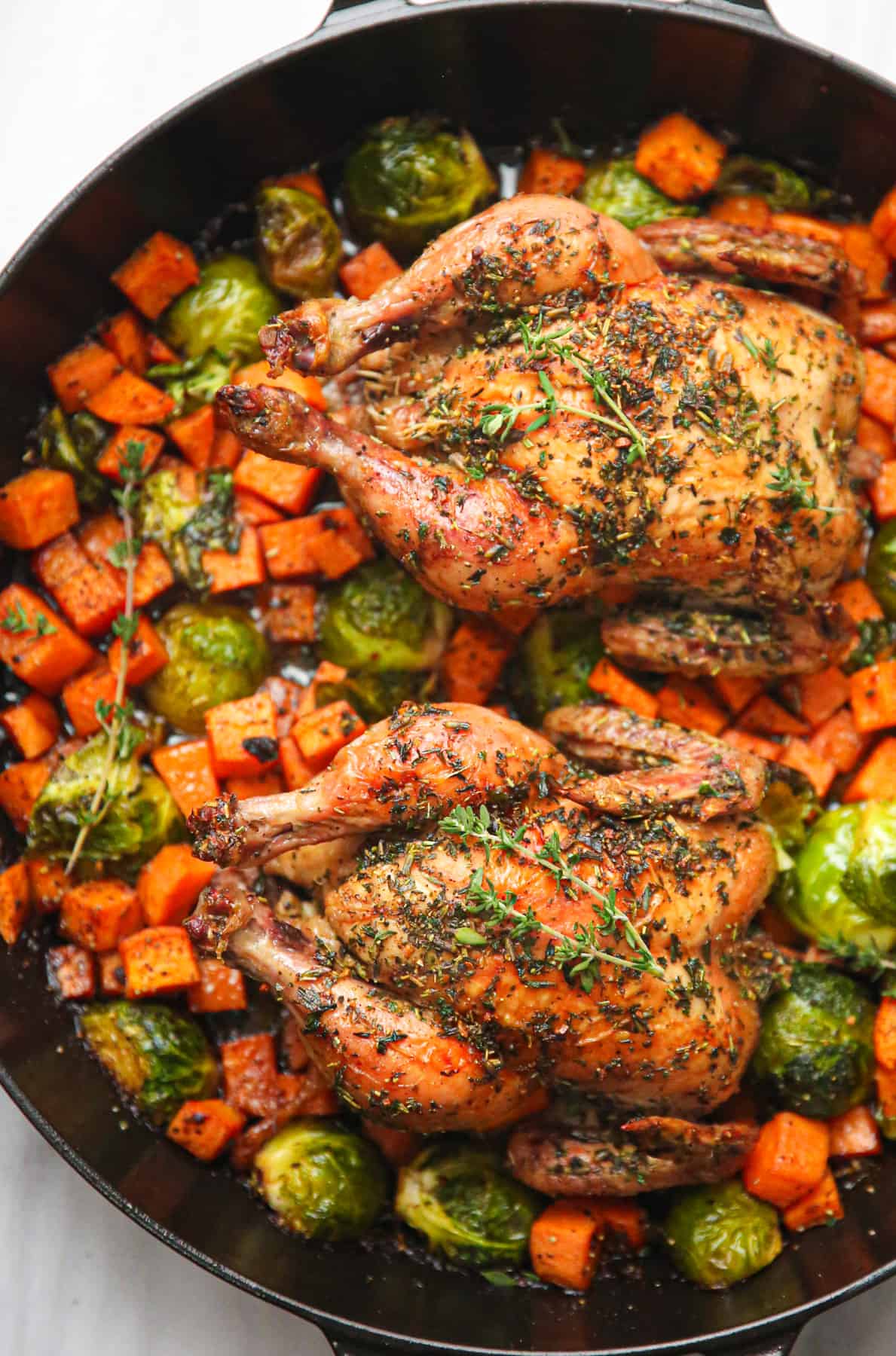 roasted Cornish hens with roasted sweet potatoes and Brussels sprouts in a cast iron pan