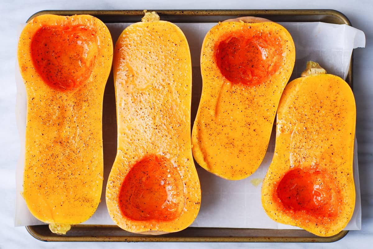 sliced butternut squash seasoned with olive oil, salt, and pepper on a parchment paper lined baking sheet