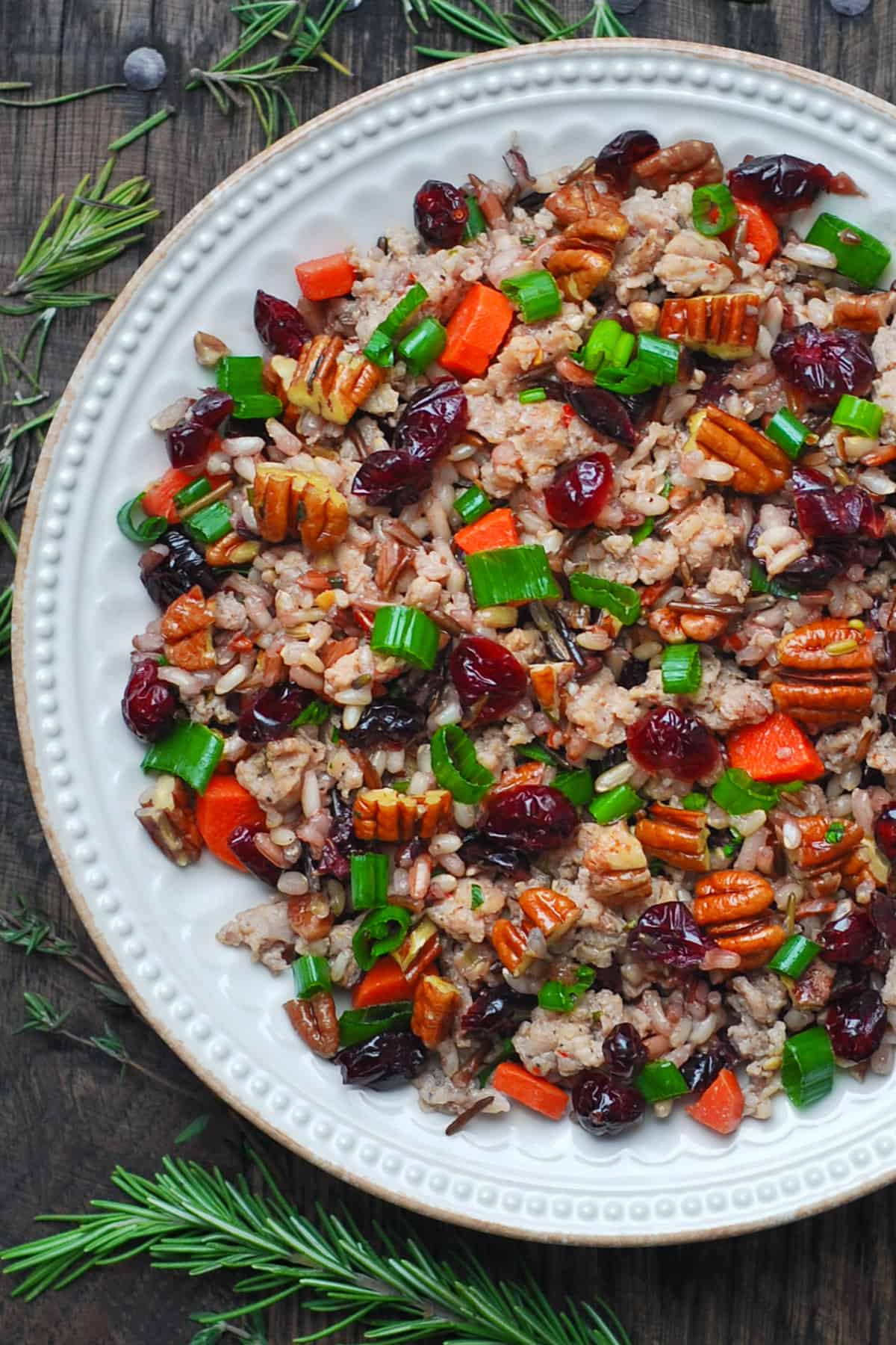 wild rice pilaf with pecans, dried cranberries, carrots, and sausage on a white plate