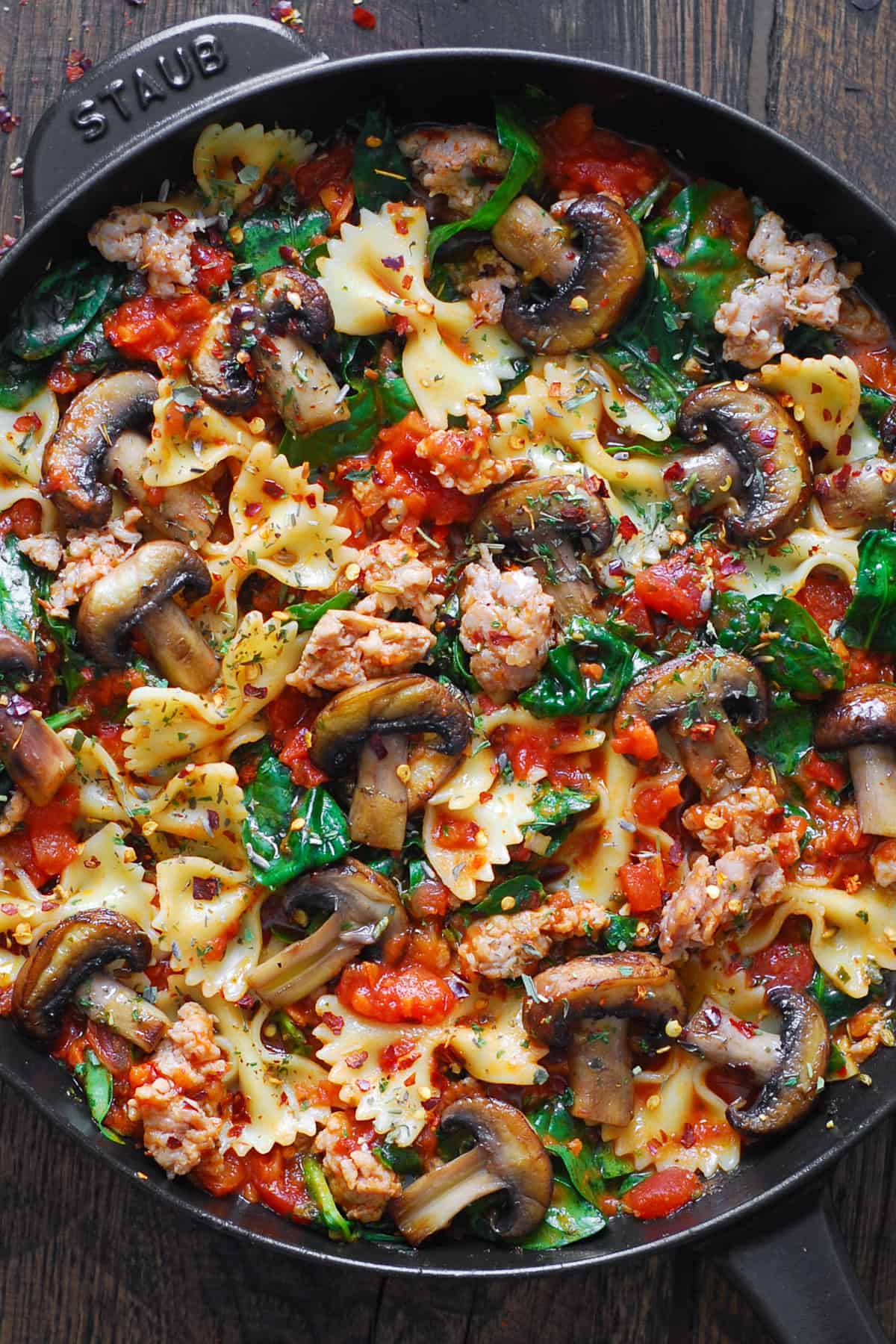 Italian sausage pasta with spinach, mushrooms, and tomato sauce in a cast iron pan