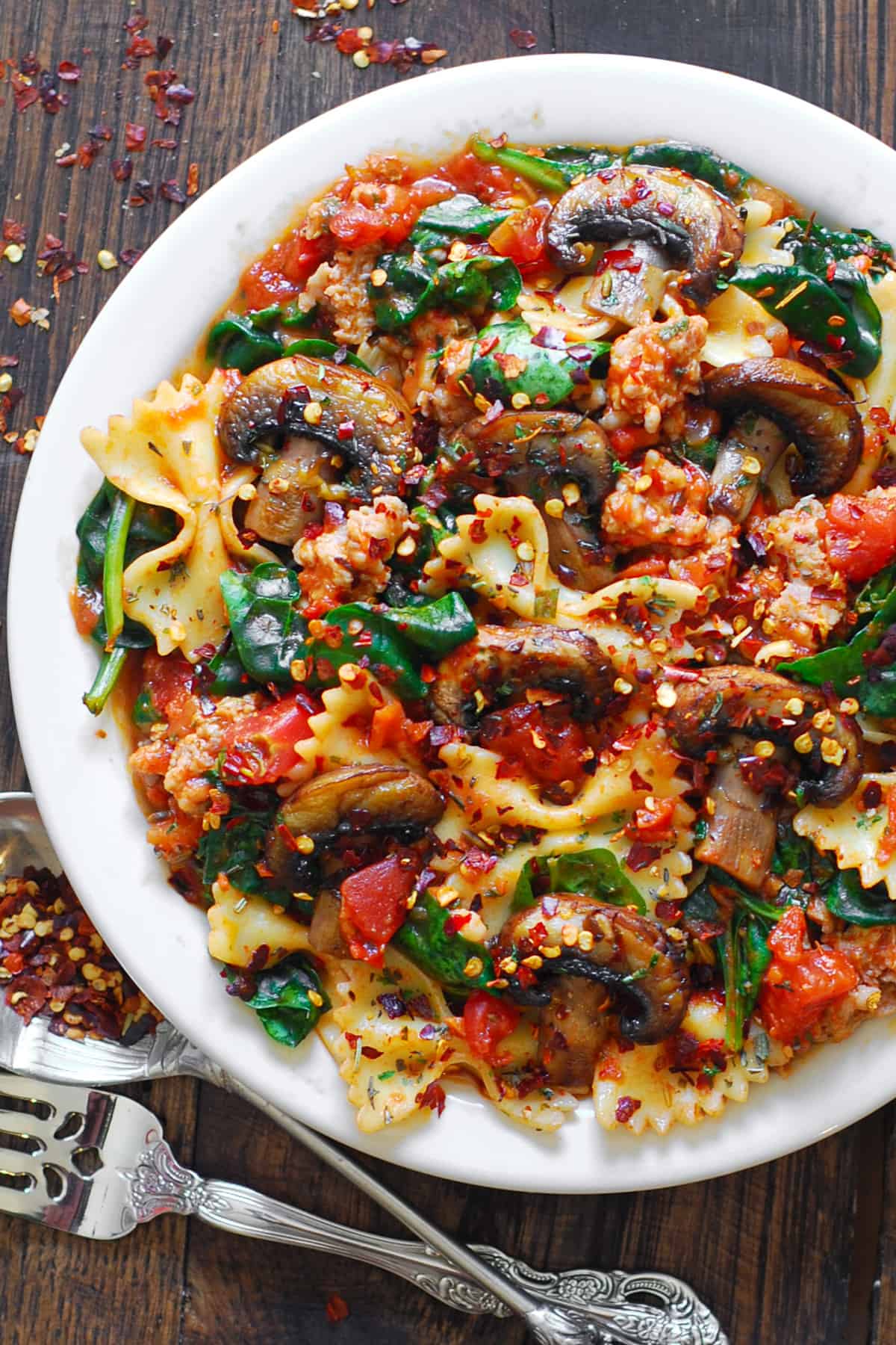 Italian sausage pasta with spinach, mushrooms, and tomato sauce on a plate