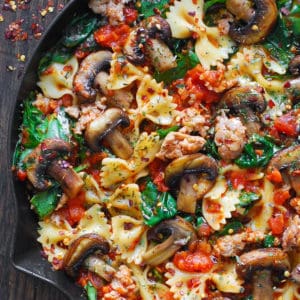 Italian sausage pasta with spinach, mushrooms, and tomato sauce in a cast iron pan