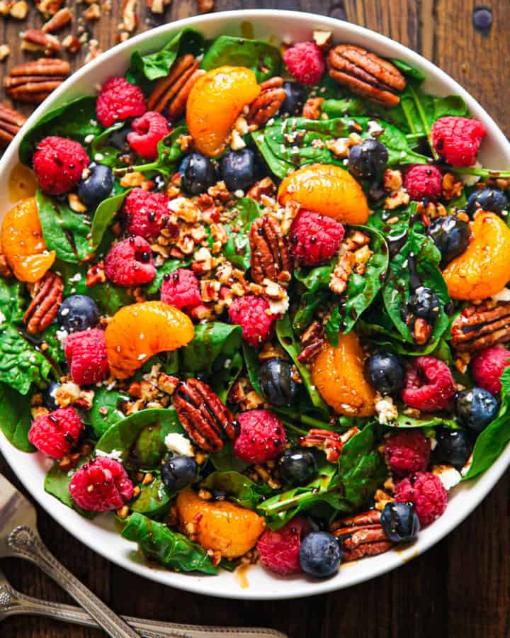 berry spinach salad with blueberries and raspberries, pecans, mandarin oranges, balsamic glaze on a plate