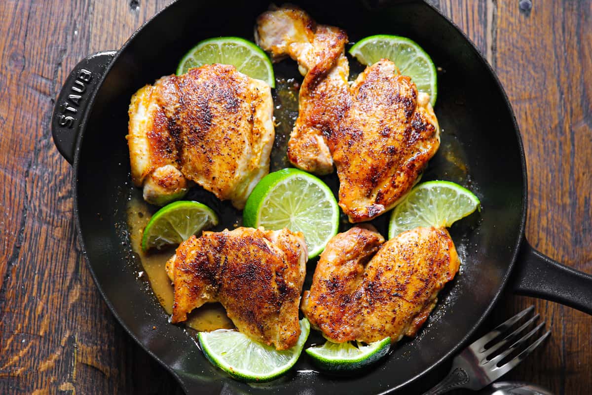 cooked chicken thighs with lime slices in a cast iron pan