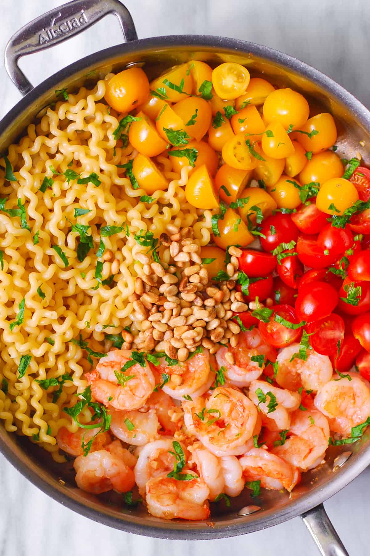 shrimp pesto pasta with roasted cherry tomatoes and pine nuts in a stainless steel pan
