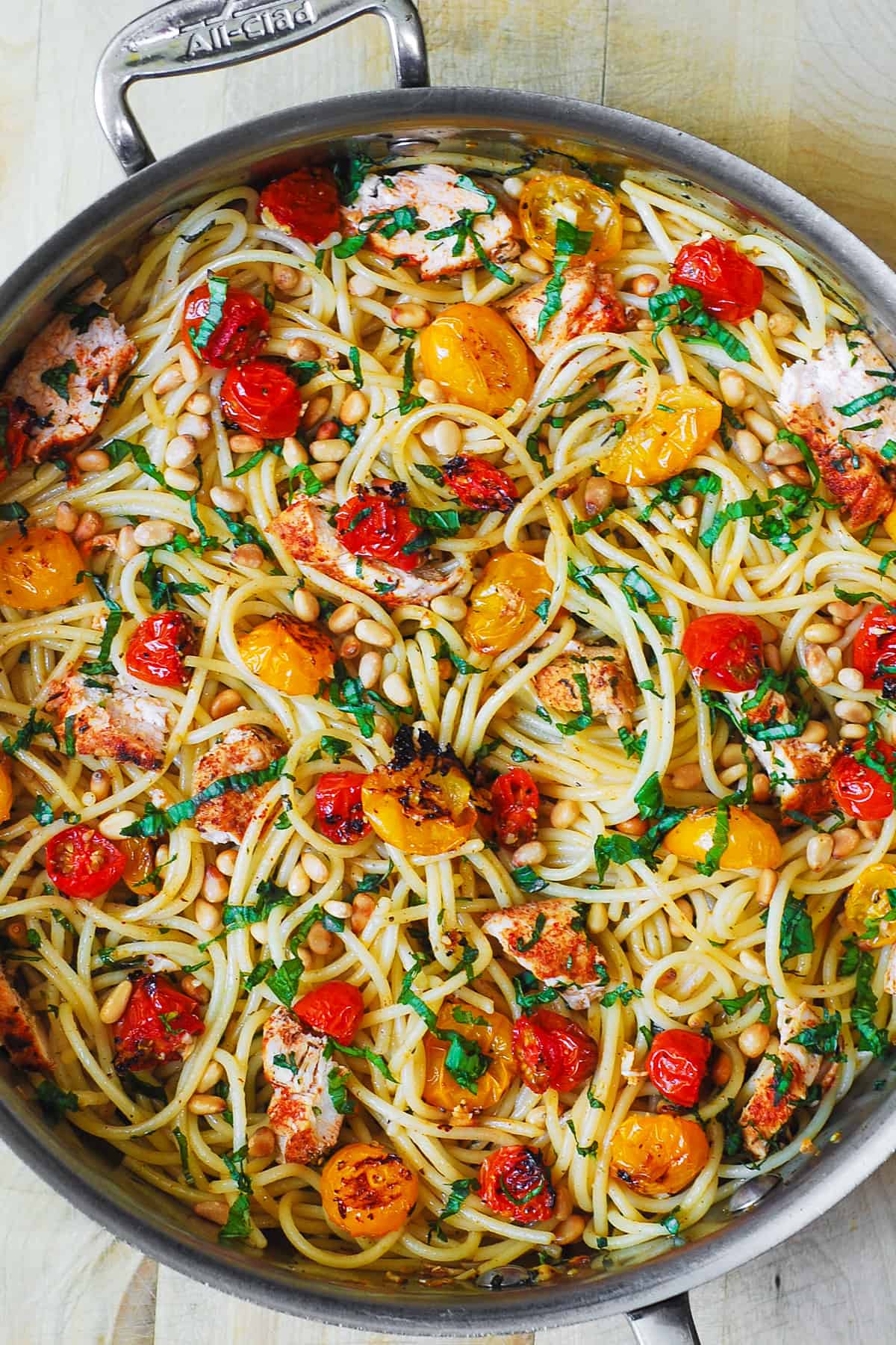 pasta with roasted cherry tomatoes, chicken, pine nuts, and lemon garlic butter sauce in a stainless steel pan