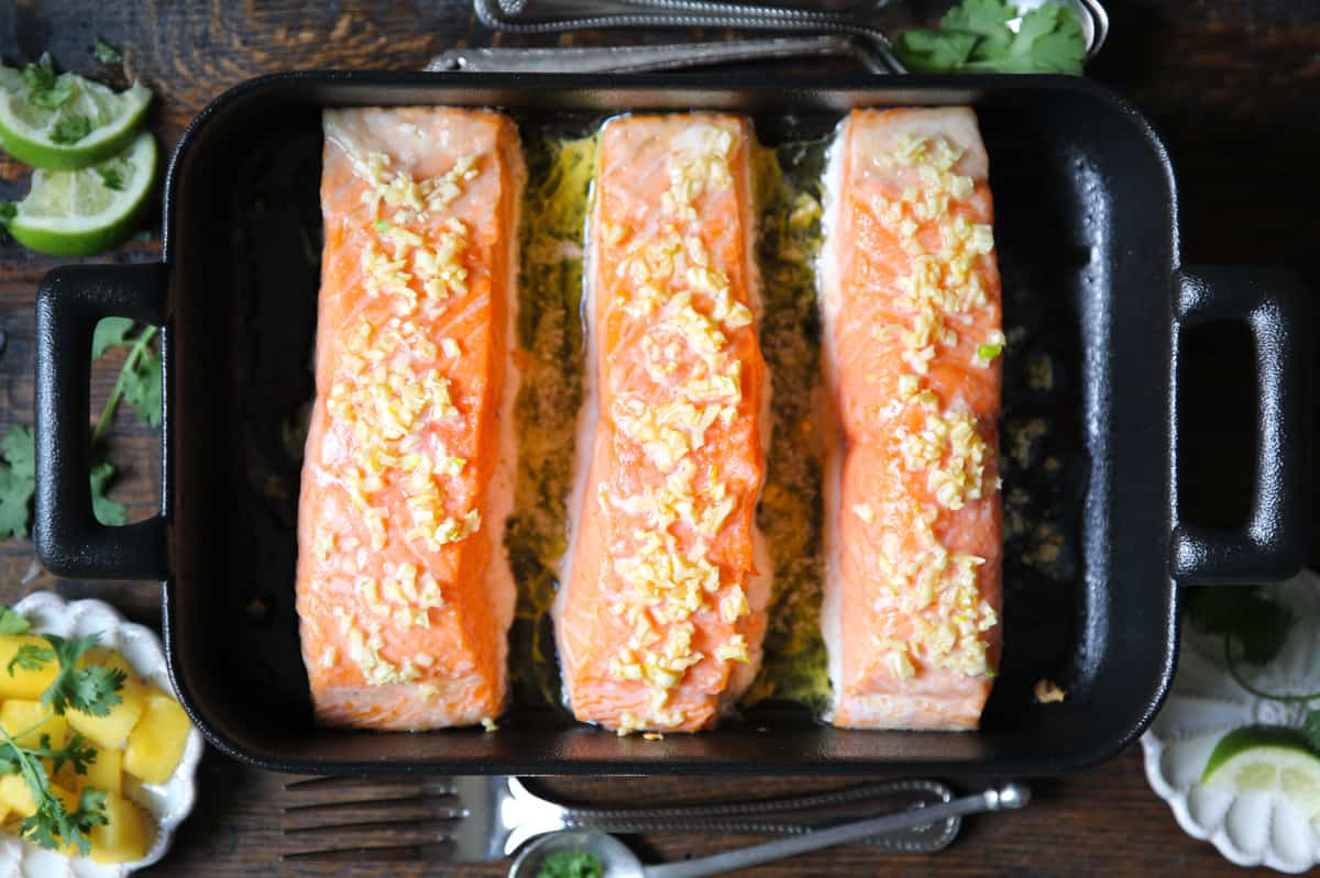 three baked salmon fillets with minced garlic and butter in a baking dish