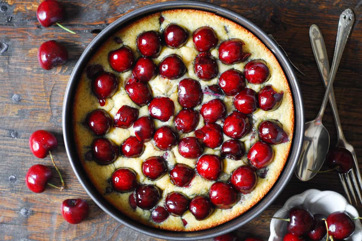 cherry cake batter baked halfway through with fresh cherries on top in a springform pan