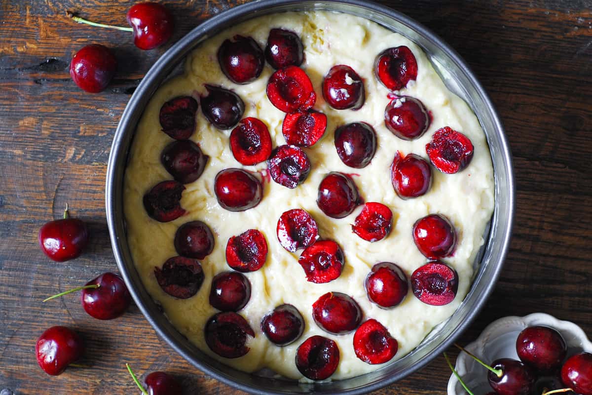 cake batter with fresh sliced and pitted cherries on top in a springform pan