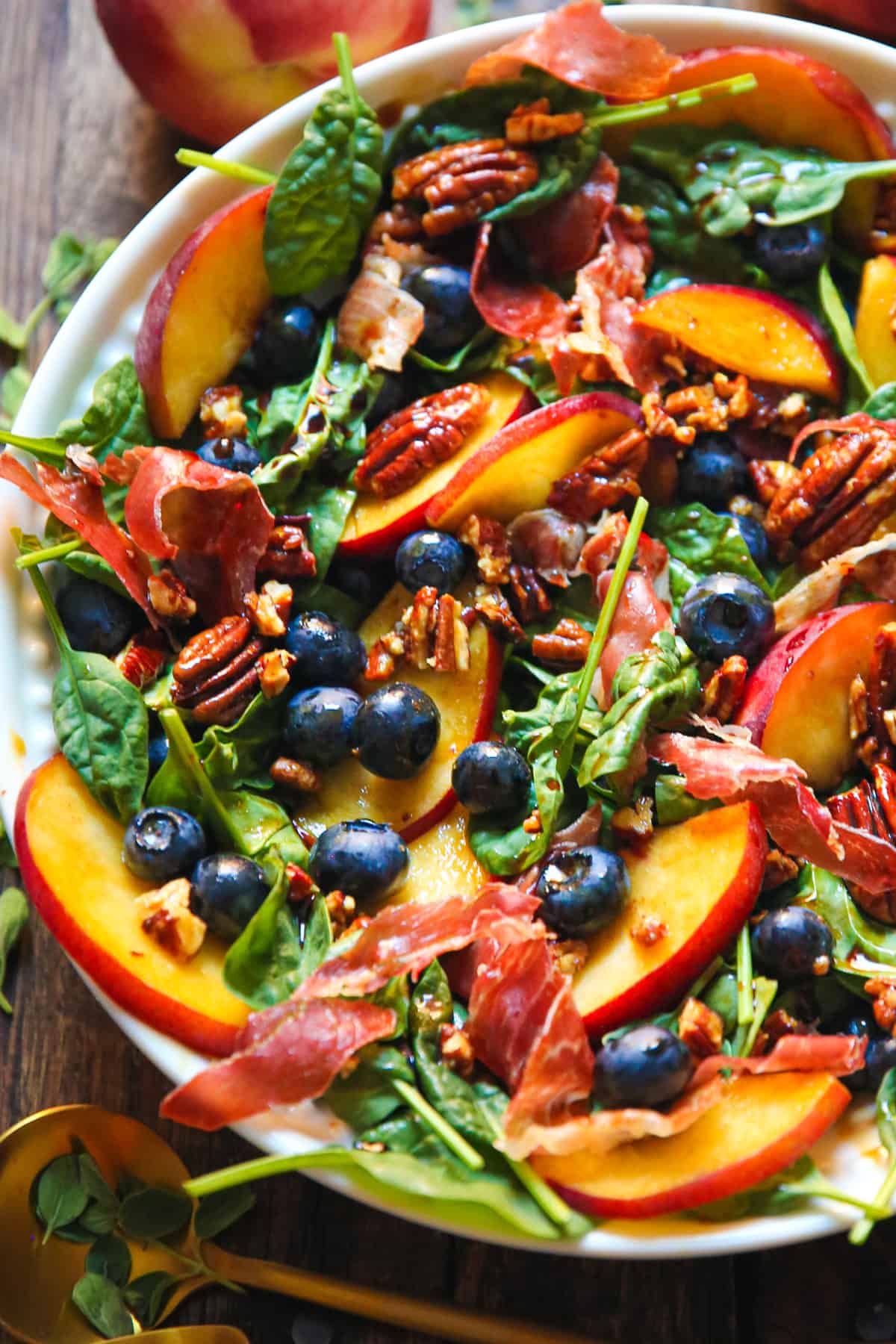 peach blueberry spinach salad with prosciutto and pecans in a bowl