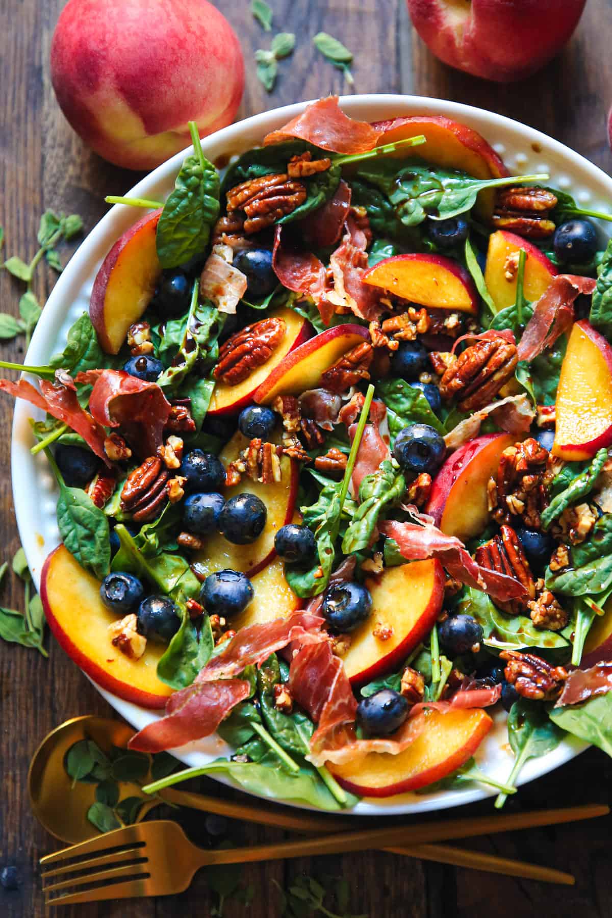 peach blueberry spinach salad with prosciutto and pecans in a bowl