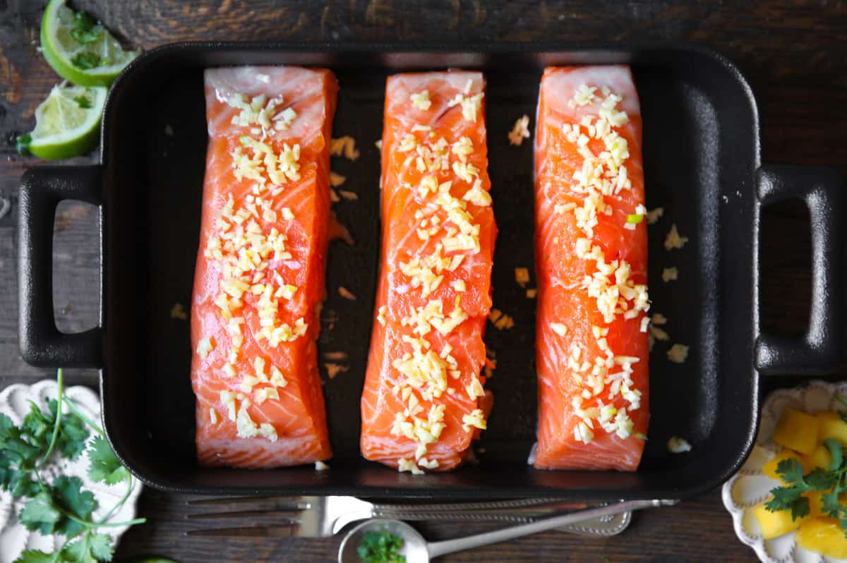 three raw salmon fillets with minced garlic in a baking dish