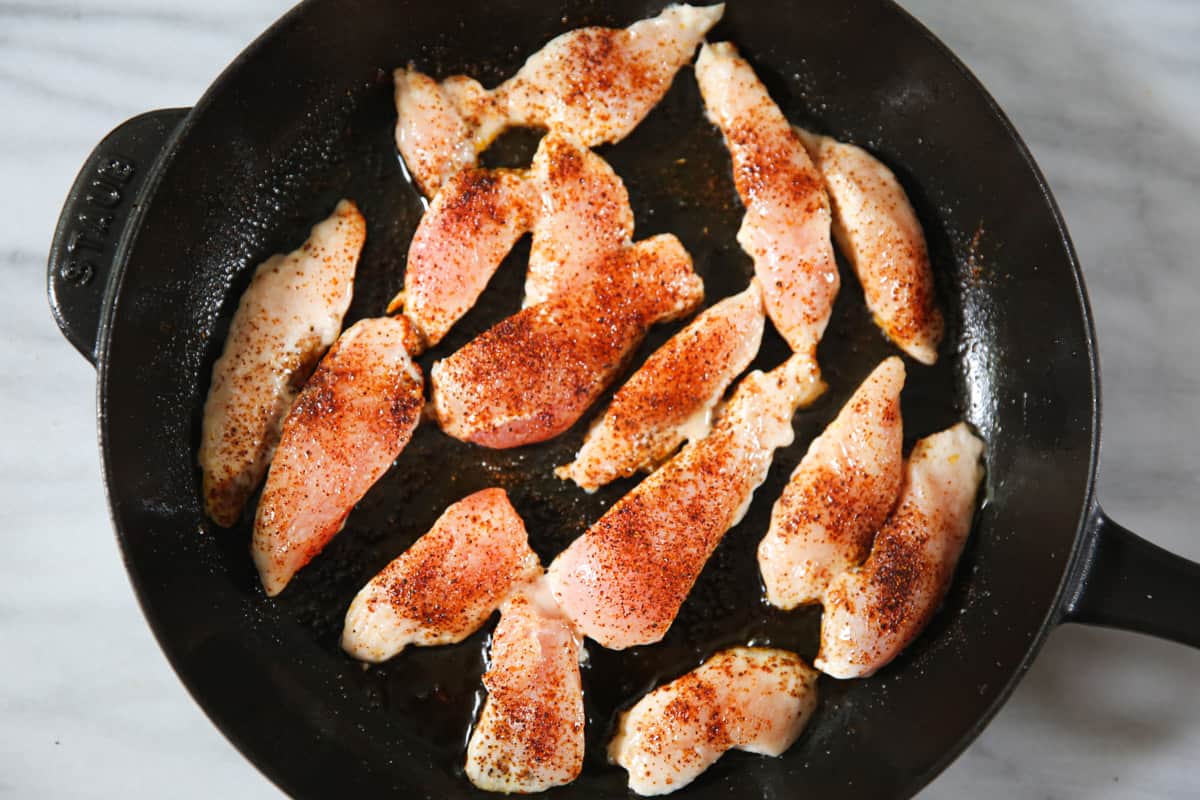 raw sliced skinless boneless chicken breasts seasoned with smoked paprika, chili powder, salt, and pepper in a cast iron skillet