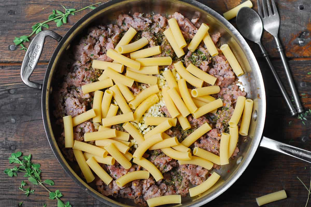 cooked sausage and uncooked rigatoni in a stainless steel skillet.