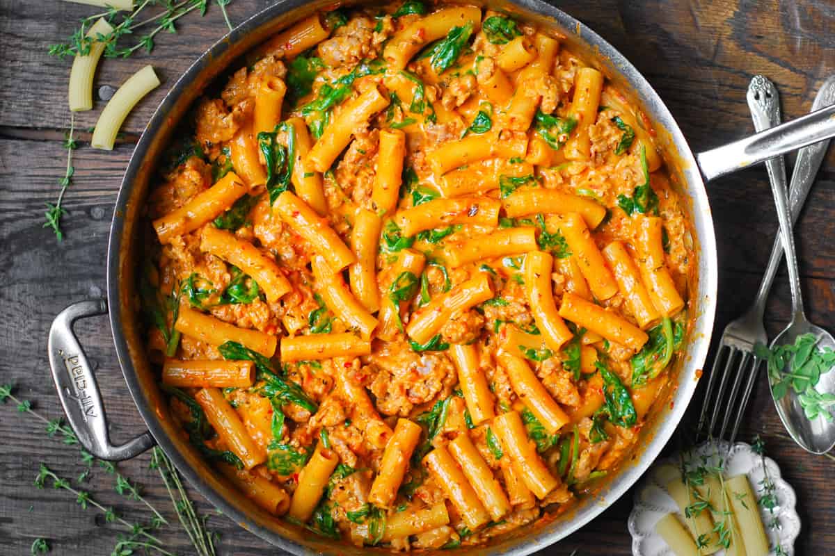 creamy sausage rigatoni with tomato sauce and spinach in a stainless steel skillet.