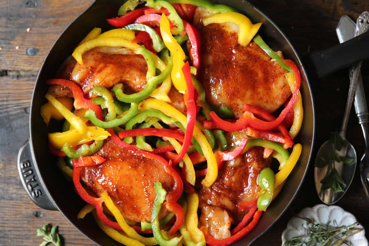 seasoned raw chicken breasts and sliced bell peppers in a cast iron skillet