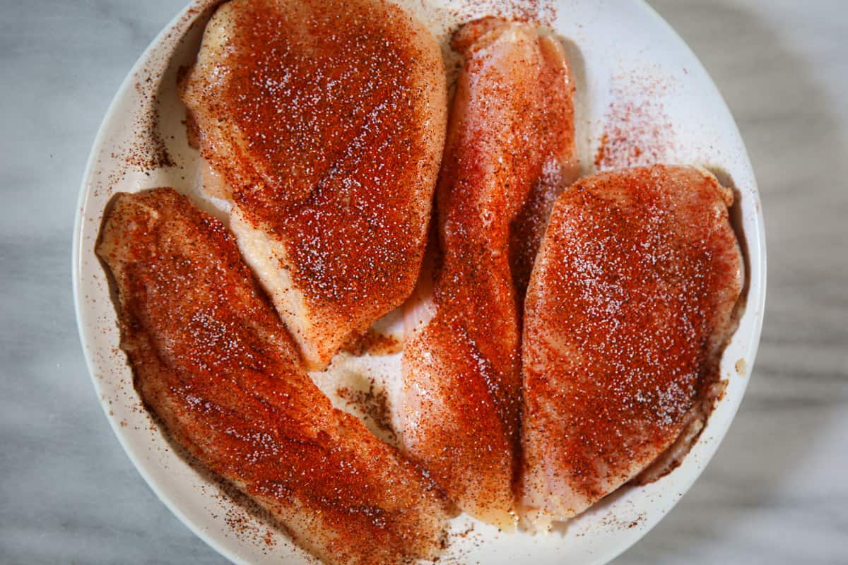 seasoned raw chicken breasts on a white plate