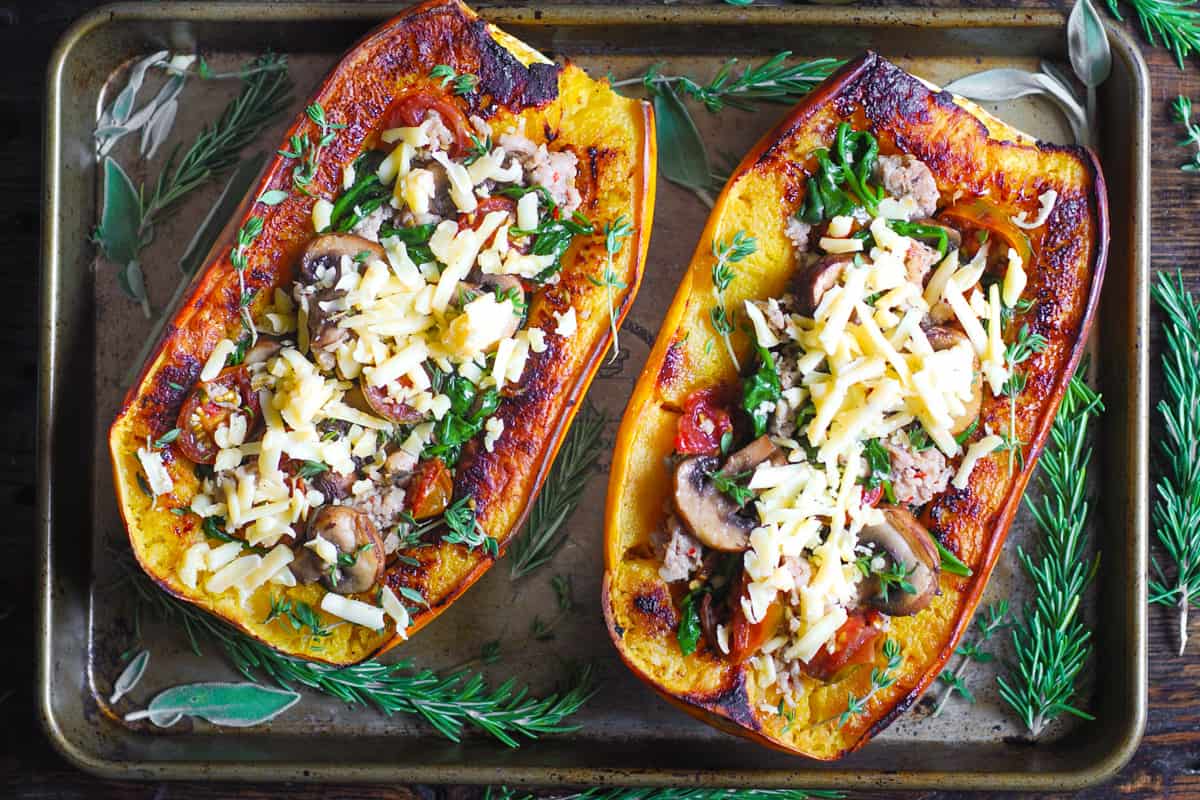 stuffed spaghetti squash with sausage, spinach, mushrooms, shredded cheese on a baking sheet.