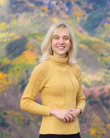 Photo of Julia (the content creator behind this website) in yellow sweater against the Autumn background.