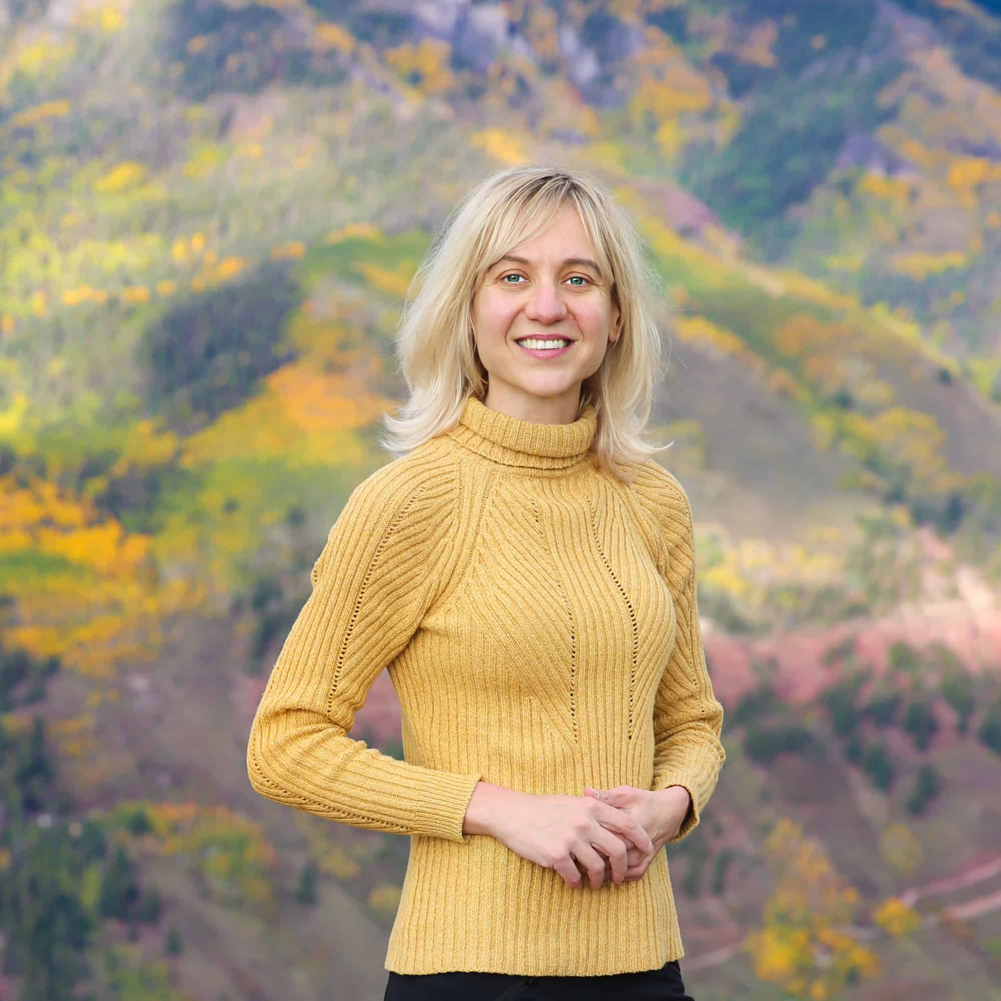 Photo of Julia (the content creator behind this website) in yellow sweater against the Autumn background.