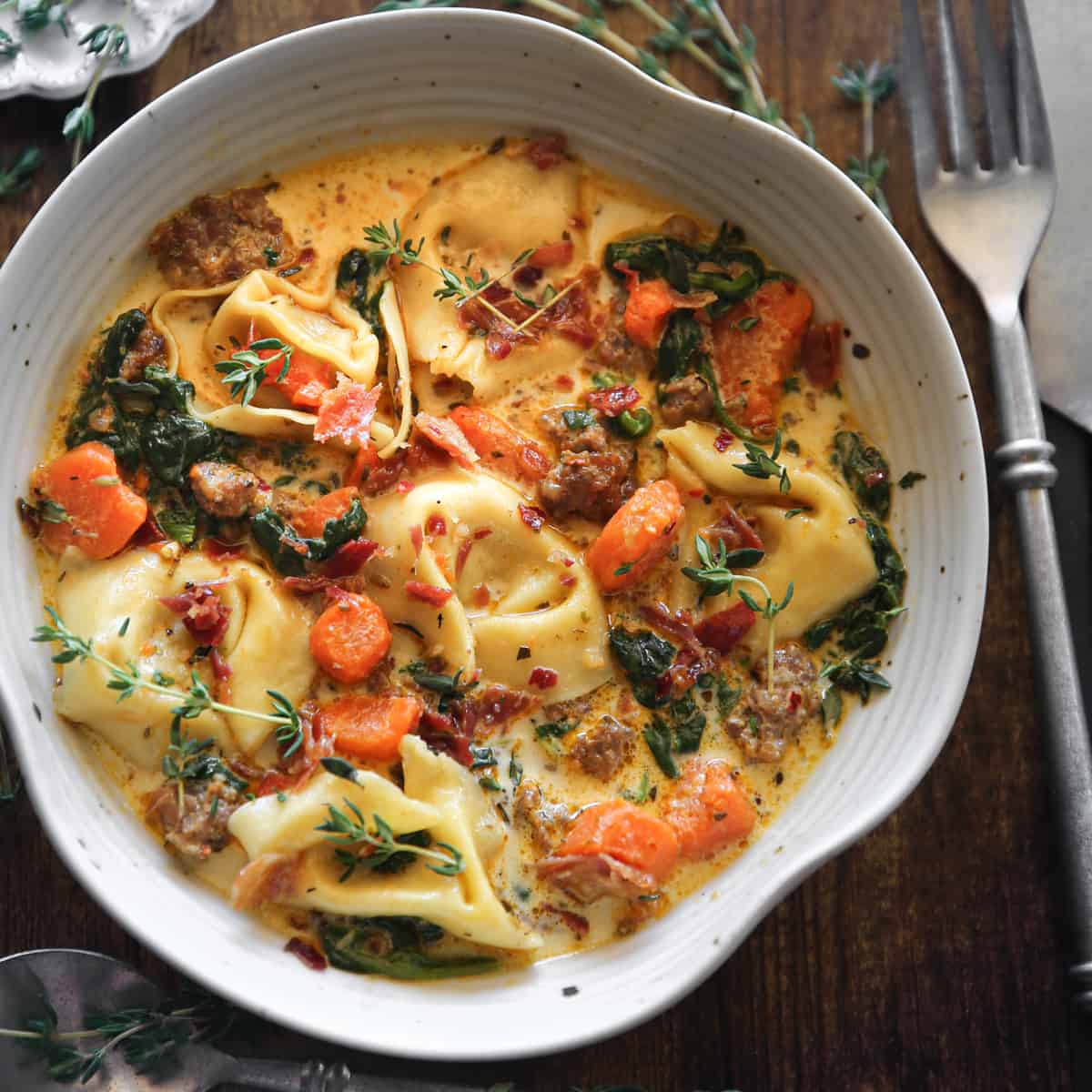 Creamy Italian Sausage Tortellini Soup with Spinach, Carrots, and Bacon Bits - in a white bowl.