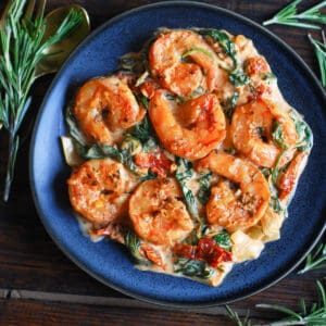 Creamy Tuscan Shrimp with Spinach, Artichokes, and Sun-Dried Tomatoes - on a blue plate.
