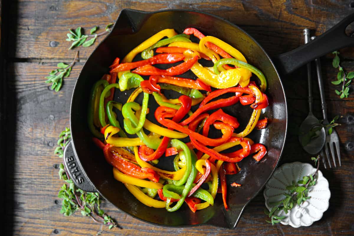 cooked sliced bell peppers (red, yellow, green) in a cast iron skillet.