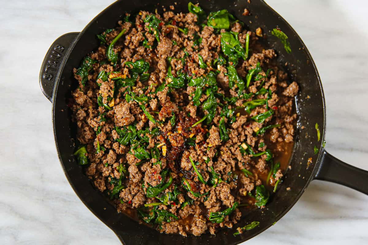 cooked ground beef and cooked spinach in a cast iron skillet.