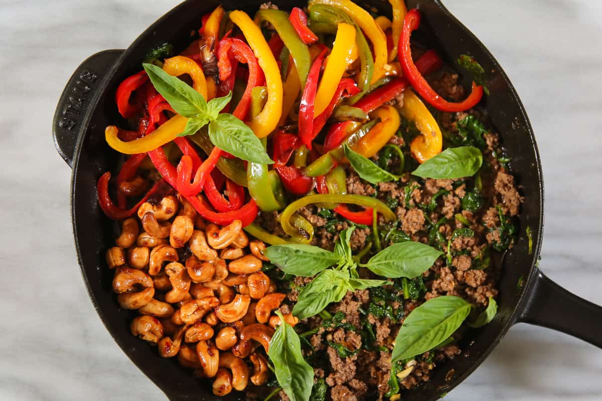 Ingredients for stir fry - cooked bell peppers, cooked ground beef and spinach, cashews - in a cast iron skillet.
