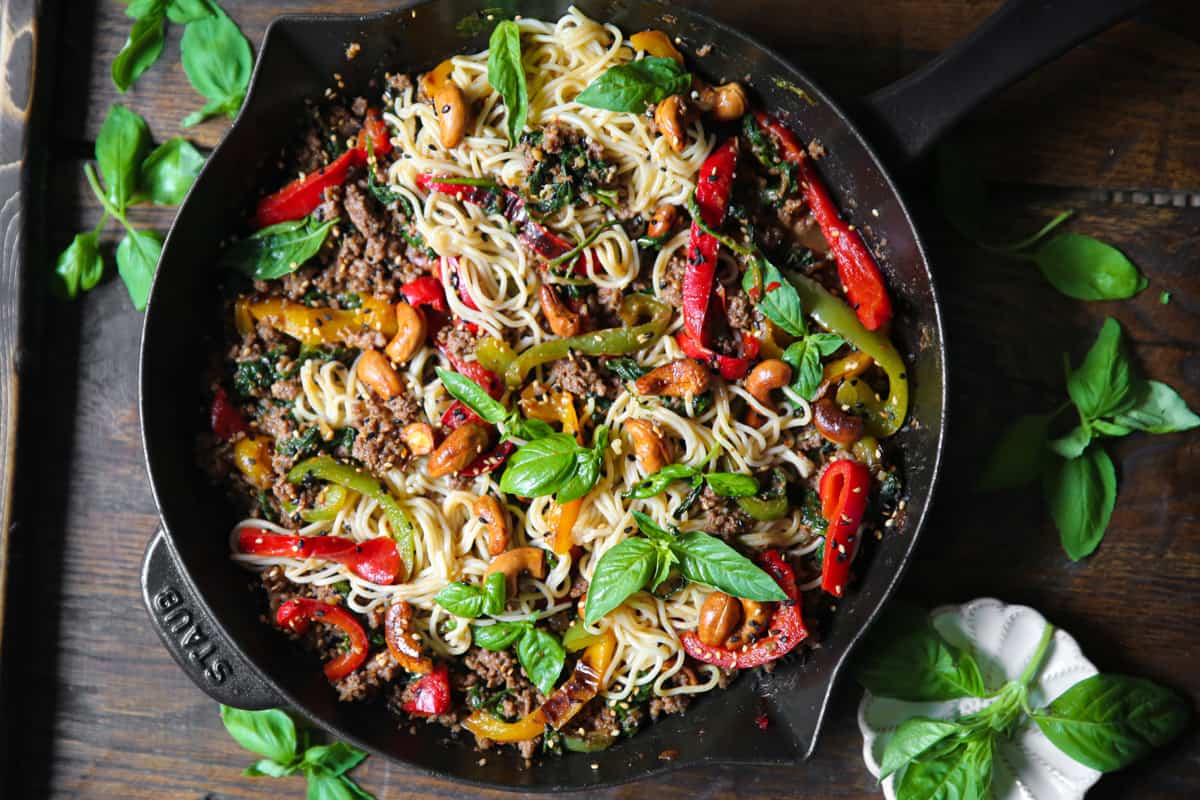 Ramen Noodles Stir Fry with Ground Beef, Bell Peppers, Spinach, Cashews, Sesame Seeds - in a cast iron skillet.