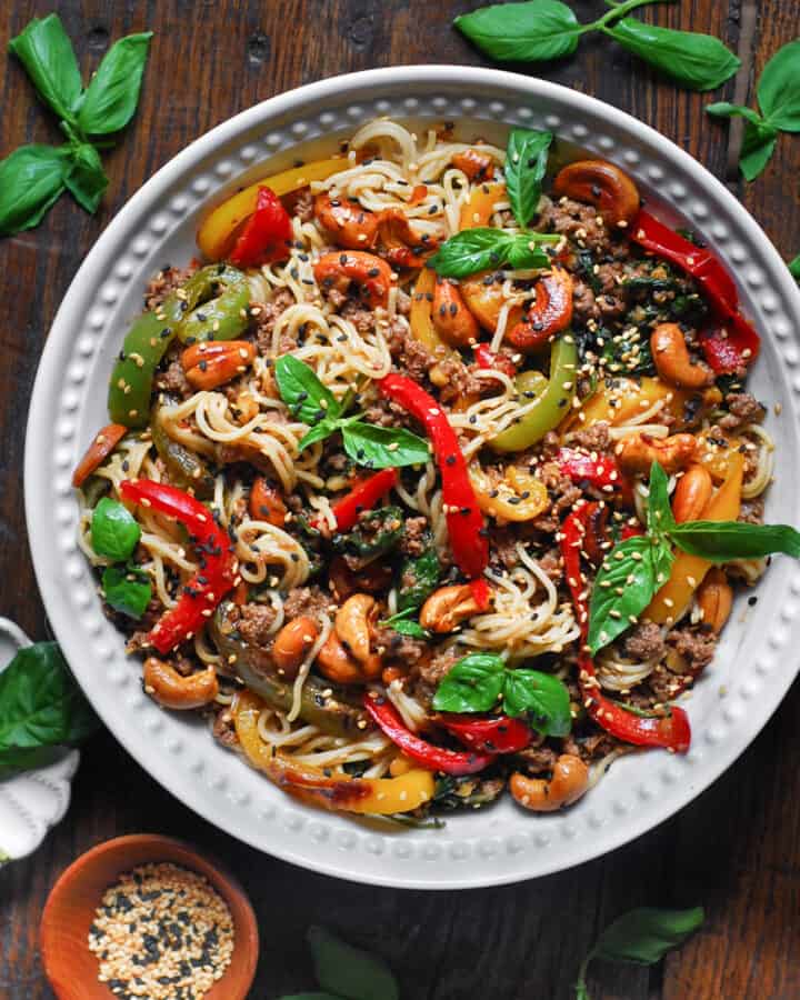 Ramen noodles stir fry with bell peppers, spinach, cashews, and ground beef - in a white bowl.