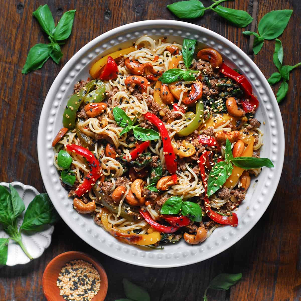 Ramen noodles stir fry with bell peppers, spinach, cashews, and ground beef - in a white bowl.