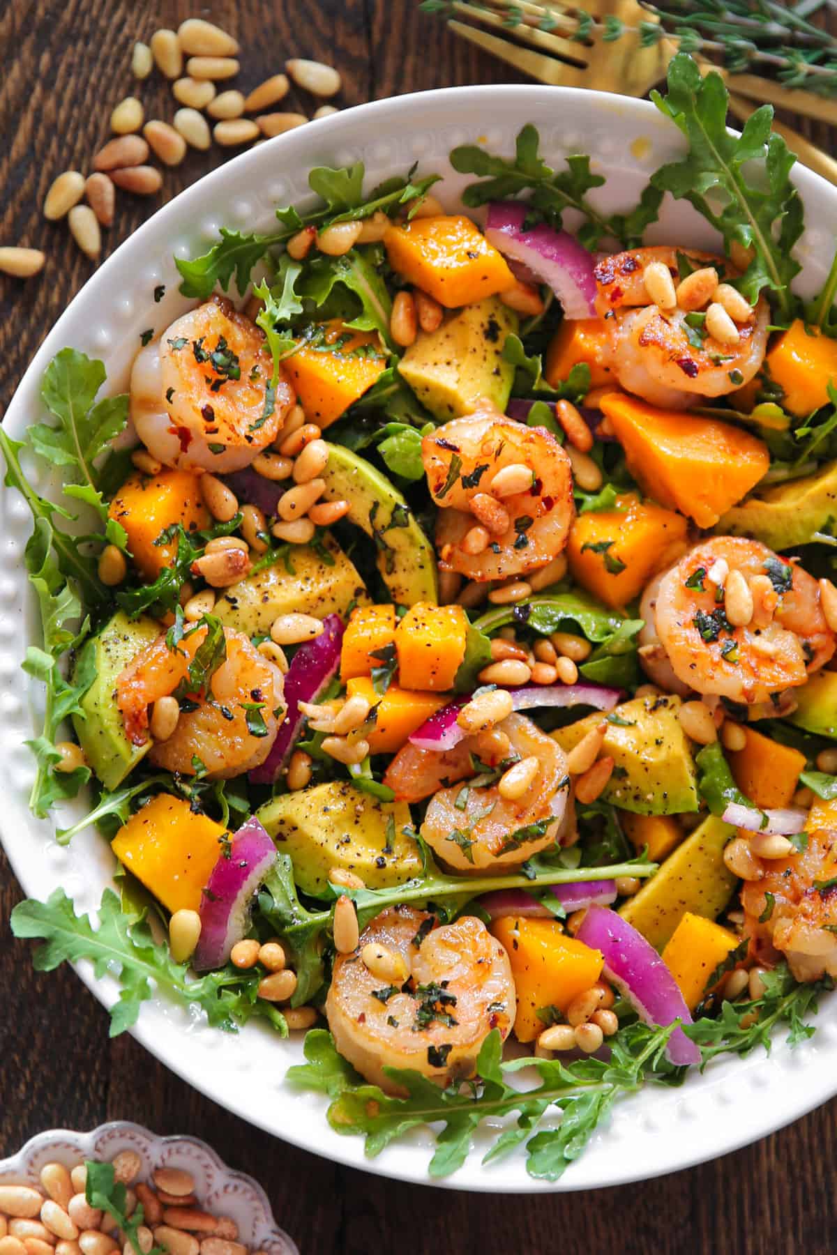 Shrimp Avocado Salad with Arugula, Pine Nuts, Mango, Red Onion - in a white bowl.