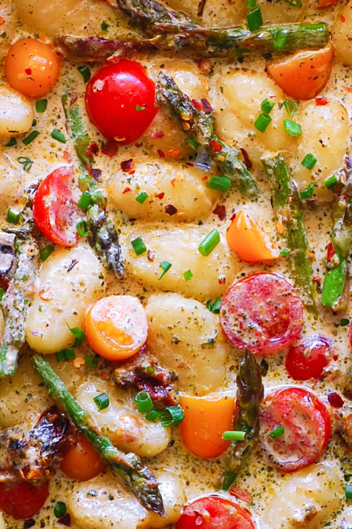 Creamy Pesto Gnocchi with Red and Yellow Cherry Tomatoes and Asparagus - close-up photo.