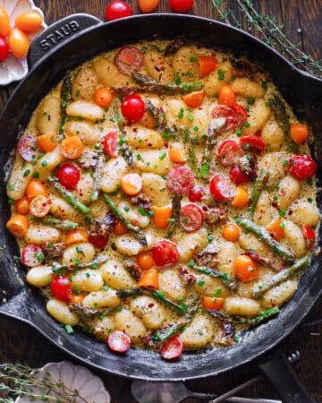 Creamy Pesto Gnocchi with Red and Yellow Cherry Tomatoes and Asparagus - in a cast iron skillet.
