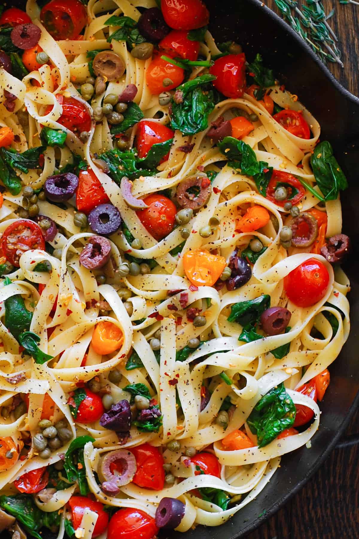 tomato spinach fettuccine pasta with olives, capers - in a cast iron skillet.