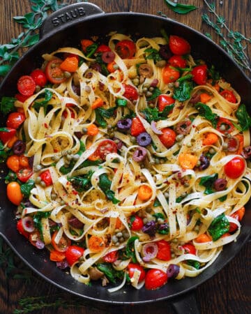 tomato and spinach fettuccine pasta with capers and olives - in a cast iron skillet.