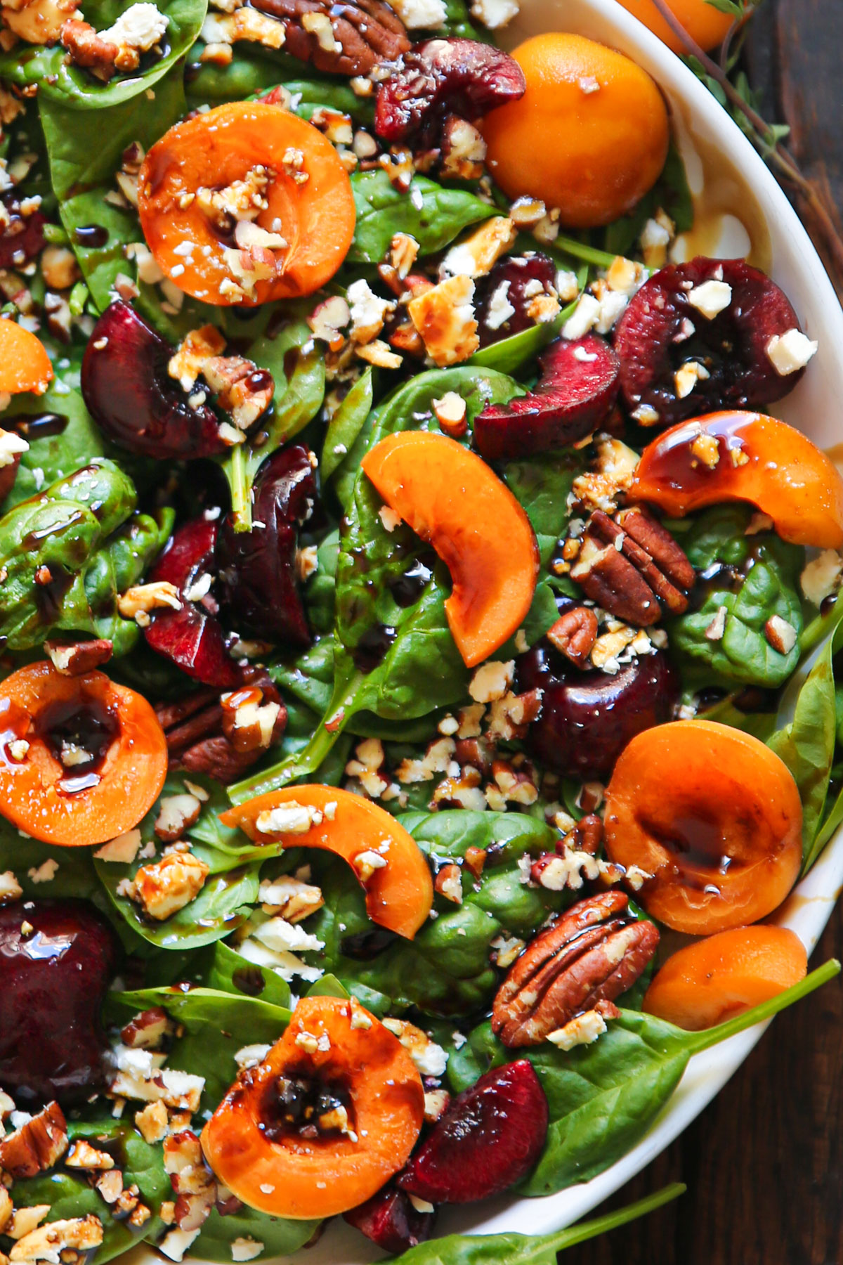 Apricot Salad with Spinach, Cherries, Pecans, Feta Cheese, and Balsamic Glaze - on a white plate.