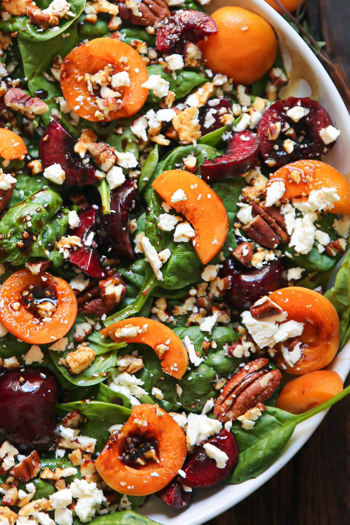 Apricot Salad with Spinach, Cherries, Pecans, Feta Cheese, and Balsamic Glaze - on a white plate.