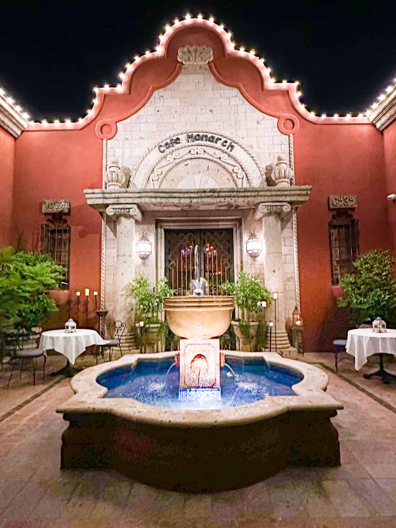the view of the Cafe Monarch Restaurant building from outside, with the fountain in the front, at night.