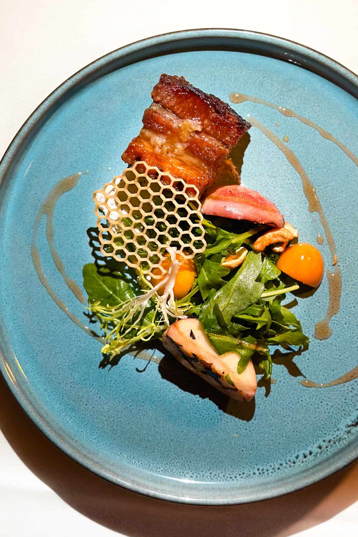 Pork Belly with Arugula, Grilled Peaches, Cashews, Goat Cheese, and Honeycomb (second course) - on a blue plate at Cafe Monarch in Scottsdale, AZ.