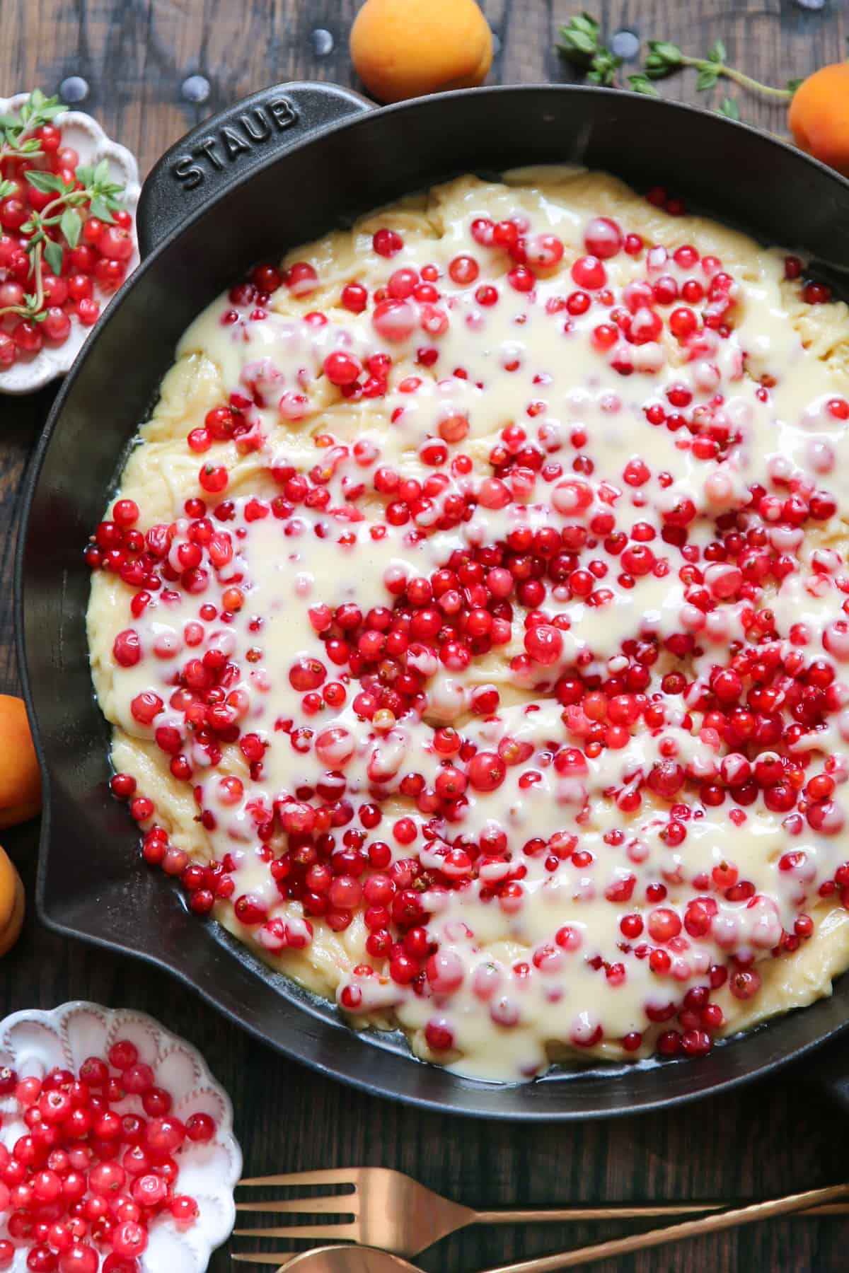 cake batter topped with cream cheese filling and red currants - in a cast iron skillet.