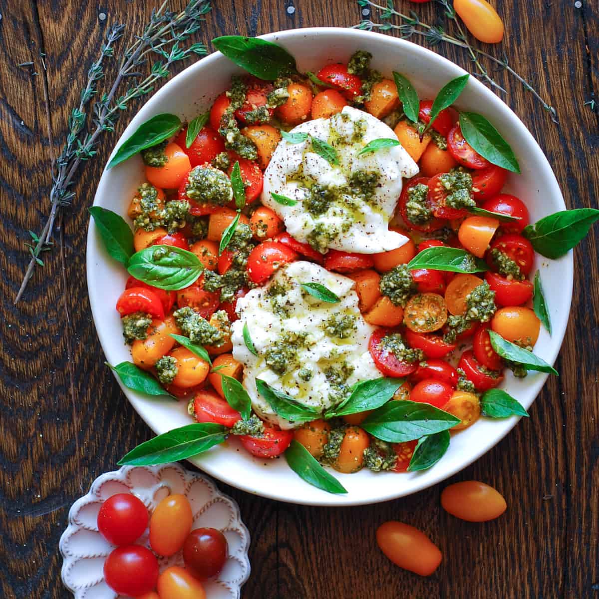 Tomato Burrata Salad with Cherry Tomatoes, Basil Pesto, and Fresh Basil Leaves - on a white plate.