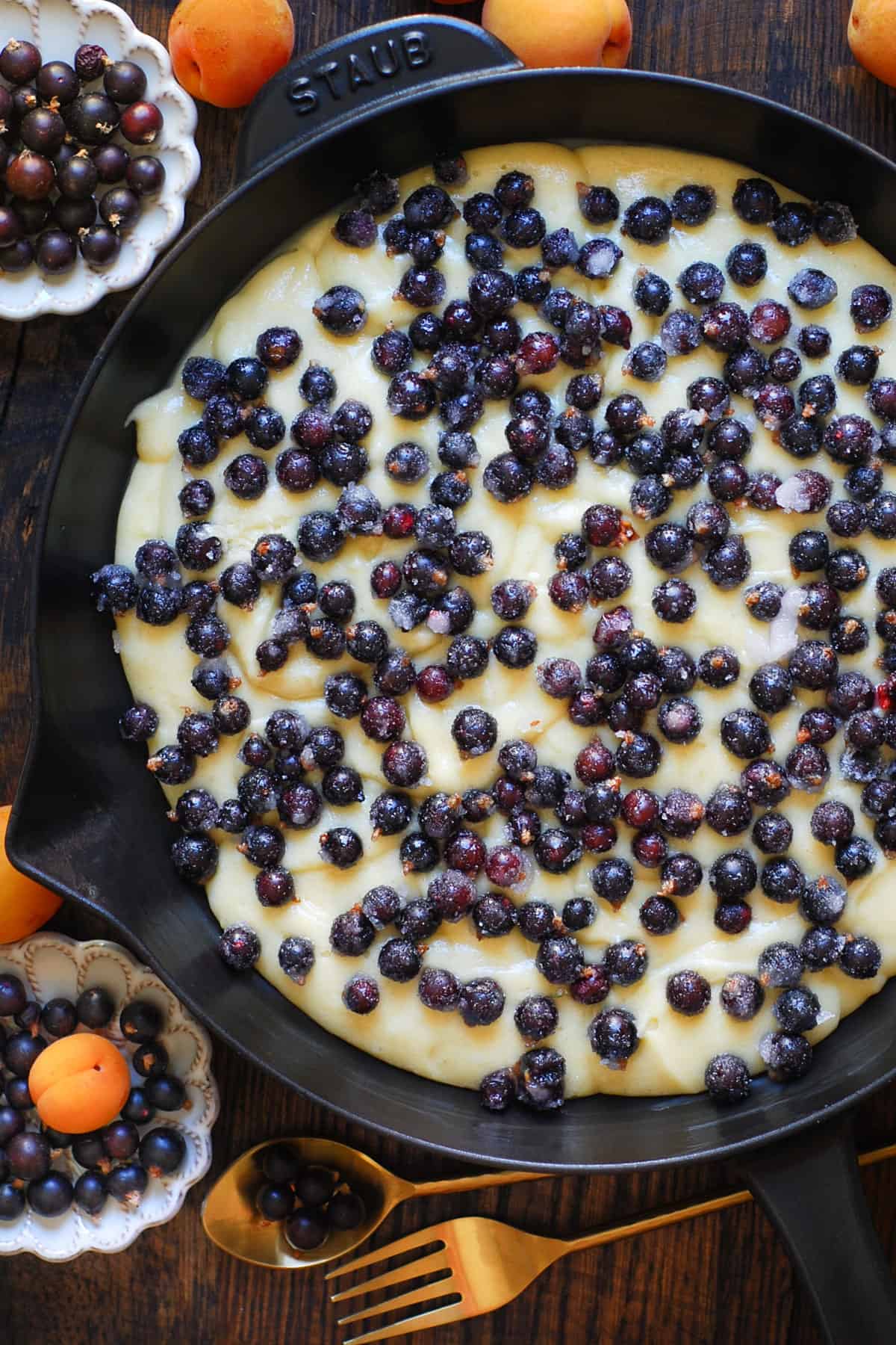 cake batter with fresh black currants on top in a cast iron skillet.