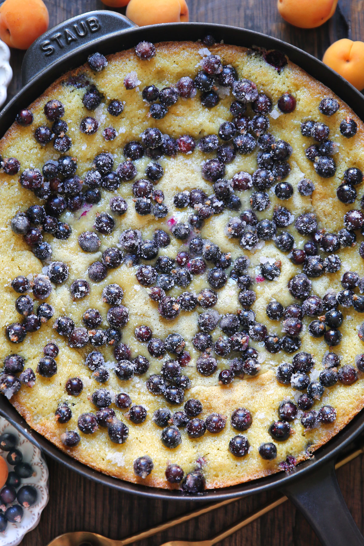 slightly baked cake batter with fresh black currants on top in a cast iron skillet.