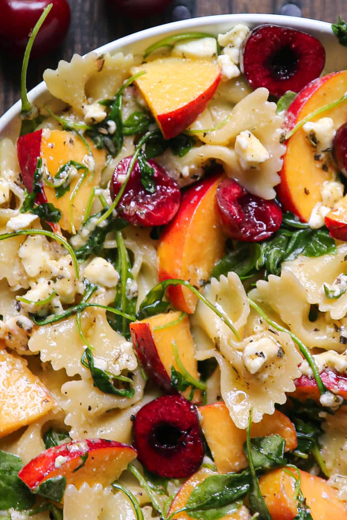 Stone Fruit Salad with Cherries, Peaches, Bow-Tie Pasta, Feta, and Arugula - in a white bowl.